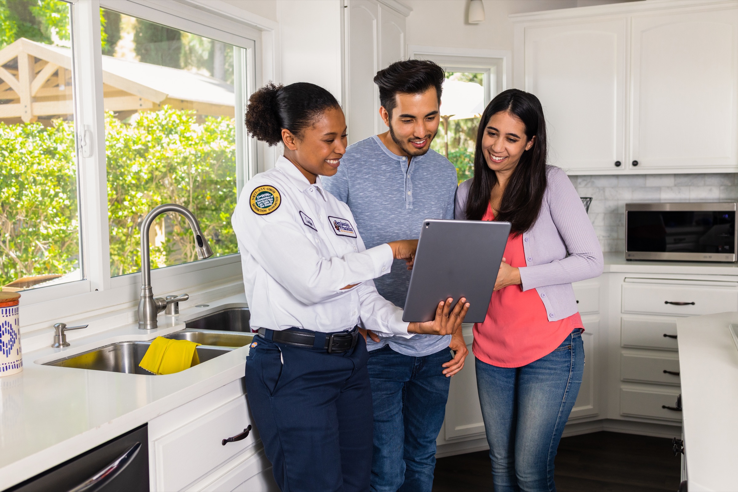 A Northern Benjamin Franklin Plumbing technician showing two Twin Cities homeowners their financing options on a tablet in their kitchen